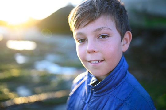Portrait of a boy with blue coat smiling outside at sunset
