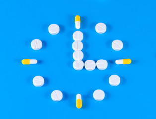 Group of different pills arranged in form of clock on blue background. Time in pharmacy.