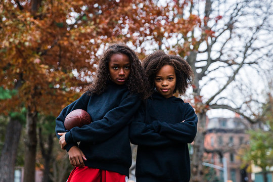 Portrait of confident sisters with American football in park