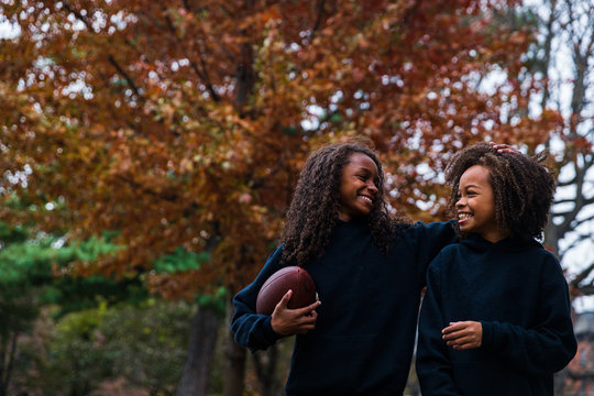 Smiling siblings with American football in park during autumn