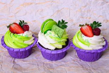 Three cupcakes with whipped cream, chocolate bar, strawberry ,decorated macaroons on crumpled paper. Picture for a menu or a confectionery catalog. with space for text.