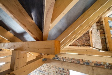 Attic of a building under construction with wooden beams of a roof structure and brick walls.