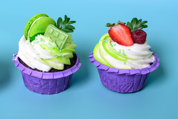 Two cupcakes with whipped cream, chocolate bar, strawberry ,decorated macaroons on blue background. Picture for a menu or a confectionery catalog. with space for text.