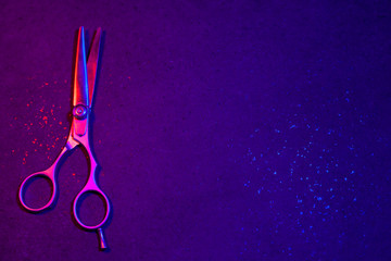 Hairdressing scissors in neon light on a dark background. The tool of the hairdresser..