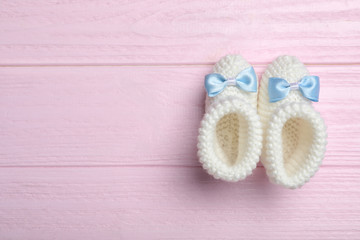 Fototapeta na wymiar Top view of child's booties on pink wooden background, space for text