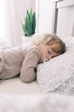 A toddler sleeping in her parents bed with a pacifier.