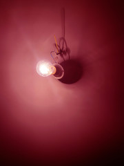 An incandescent lamp illuminates a white wall in the dark. Electricians wires on the wall. Dark room with a lamp.