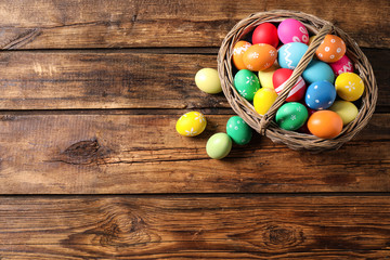 Colorful Easter eggs in basket on wooden background, flat lay. Space for text
