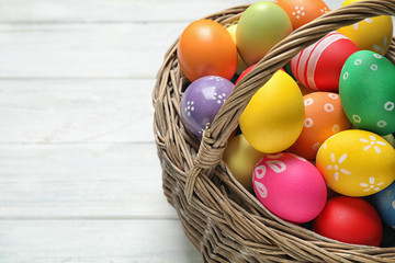 Colorful Easter eggs in basket on white wooden table, closeup. Space for text