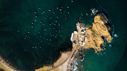 Aerial view of many fishing boats next to peninsula at the rocky coast of Peru. Little fishing...