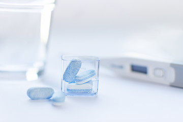 Blue pills on white background with thermometer. Traditional medicine treatment.