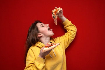 young happy girl eating pizza on a colored background, a teenager holds two slices of pizza and eat...