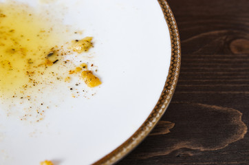 Food leftovers after meal. Yellow fat with spices on a single white plate. Wooden table background. Closeup shot