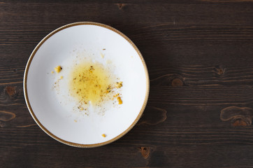 Food leftovers after meal. Yellow fat with spices on a single white plate. Wooden table background. Top down flat photo with copy space