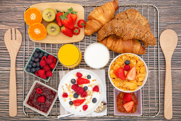 Fototapeta na wymiar Breakfast Served in the morning with Fruit Yogurt, Butter croissant and corn flakes Whole grains and raisins with milk in cups and Strawberry, Raspberry, Kiwi, Fresh Orange Juice on the breakfast