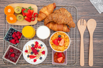 Breakfast Served in the morning with Fruit Yogurt, Butter croissant and corn flakes Whole grains and raisins with milk in cups and Strawberry, Raspberry, Kiwi, Fresh Orange Juice on breakfast table