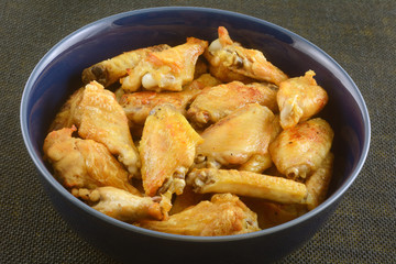 Golden brown baked chicken wings in large blue bowl on table