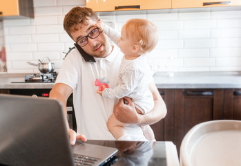 Handsome young man working at home with a laptop with a baby on his hands. Stay home concept. Home office with kids.