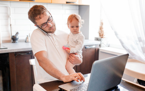 Handsome young man working at home with a laptop with a baby on his hands. Іtay home concept. Home office with kids.