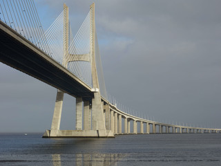 The Vasco de Gama Lisbon Bridge crosses the river Tejo, which is reflected in the sunlit water.