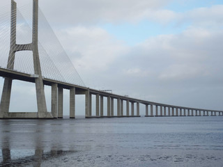 Obraz premium Bridge Vasco de Gama Lisbon crossing the river Tejo reflected in the water on a cloudy day.