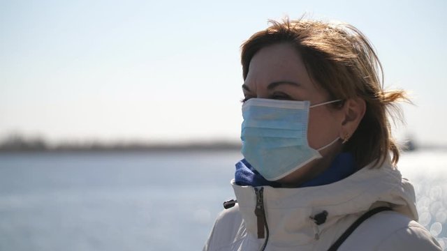 Smart blonde woman in a protective mask standing on Dnipro quay in spring