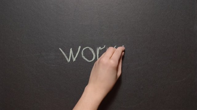 Don't worry be happy. A left female hand writes the expression "Don't worry be happy" by color chalk on a black board. Each word is written in turn