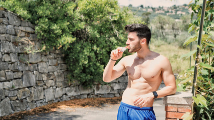 Young muscular shirtless man eating protein bar outdoor in a street in summer