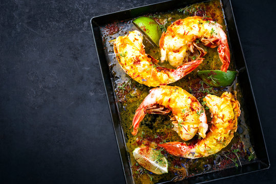 Traditionell gegrillte Langusten Schw&auml;nze  aufgeschnitten und angeboten mit Safran Zitronen Sauce als Draufsicht auf einem Metall Tablett mit Textfreiraum links