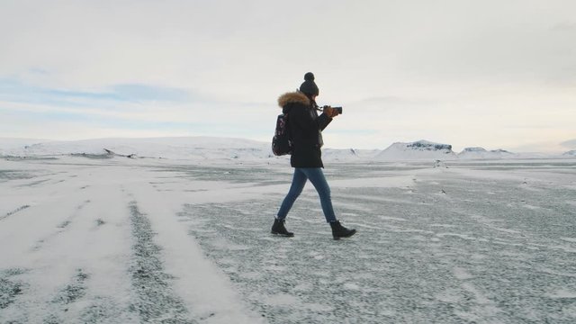 Young beautiful woman traveler with camera walking on snow desert in Iceland. Slow motion shot at sunset or sunrise. Around Solheimasandur dc3 Plane crash area 