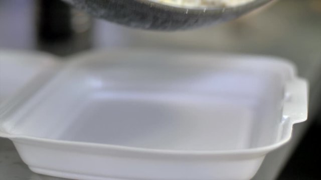 Selective focus and close up of street food, stir-fried morning glory being placed on top of white rice in a styrofoam container - environmental and heath concern