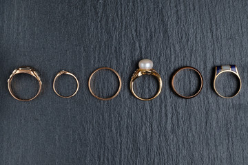 A set of different golden rings on a black stone board. Top view.