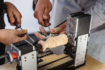 Two workers chisels grind a wooden workpiece on a lathe.