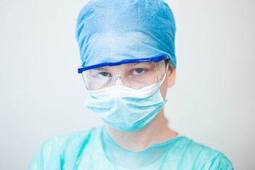 Female doctor in uniform, glasses and mask works concentrated in the hospital. portrait of a surgeon.