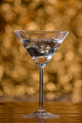 olive falling in martini glass on gold background