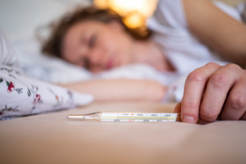 woman  in bed with fever focus on thermometer coronavirus or COVID-19 sympthoms
