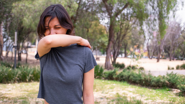 mujer joven estornudando en codo