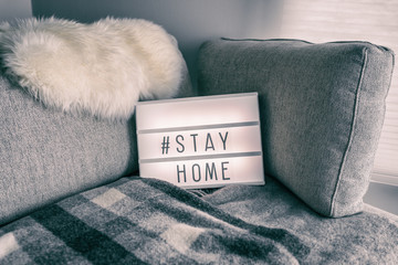 Coronavirus home lightbox sign with hashtag message #STAYHOME glowing on home sofa with cozy...