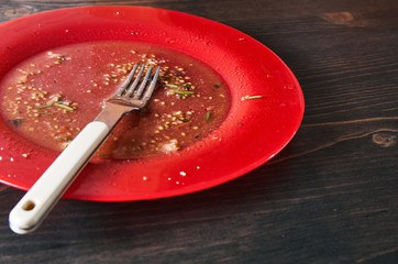 Salad leftovers after meal. Oil, tomato seeds, chopped parsley on a single red plate with white...