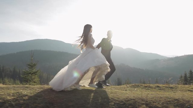 Newlyweds. Caucasian groom with bride running on mountain slope. Wedding couple