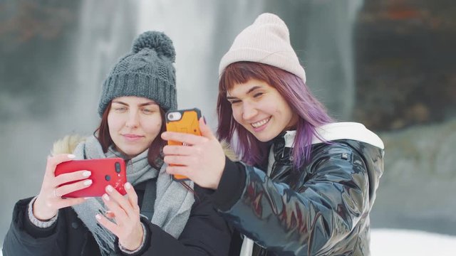 Two young beautiful girlfriends takes a selfie on the background of a waterfall Selanjafoss, Iceland