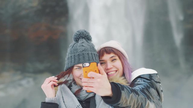Two young beautiful girlfriends takes a selfie on the background of a waterfall Selanjafoss, Iceland