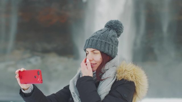 young beautiful woman takes a selfie on the background of a waterfall Selanjafoss, Iceland