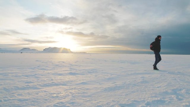 Young man traveler walking on snow desert in Iceland. Slow motion shot at sunset or sunrise. Around Solheimasandur dc3 Plane crash area 
