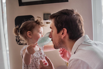 Little daughter dresses dad with a medical mask. Caring for each other in the family. Life in quarantine.