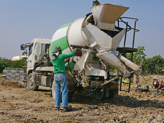 A male worker washing / cleaning a cement mixer truck after finish pouring out the concrete