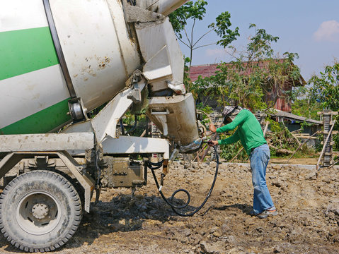 A male worker washing / cleaning a cement mixer truck after finish pouring out the concrete