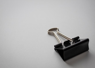 black binder clip paper clip on white paper background in the bottom right corner with empty negative space