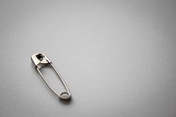 metal silver safety pin on white paper background in bottom left corner with negative space 