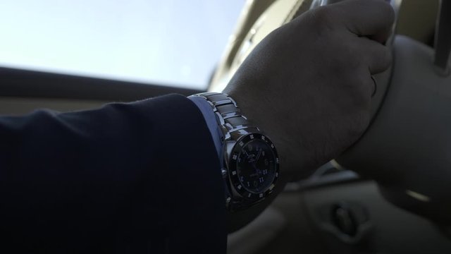 Close-up Hand Watch on Male Hand Gripping Turning Steering Wheel of Luxury Business Class Car. Young Successful Confident Businessman Driving on Urban Highway